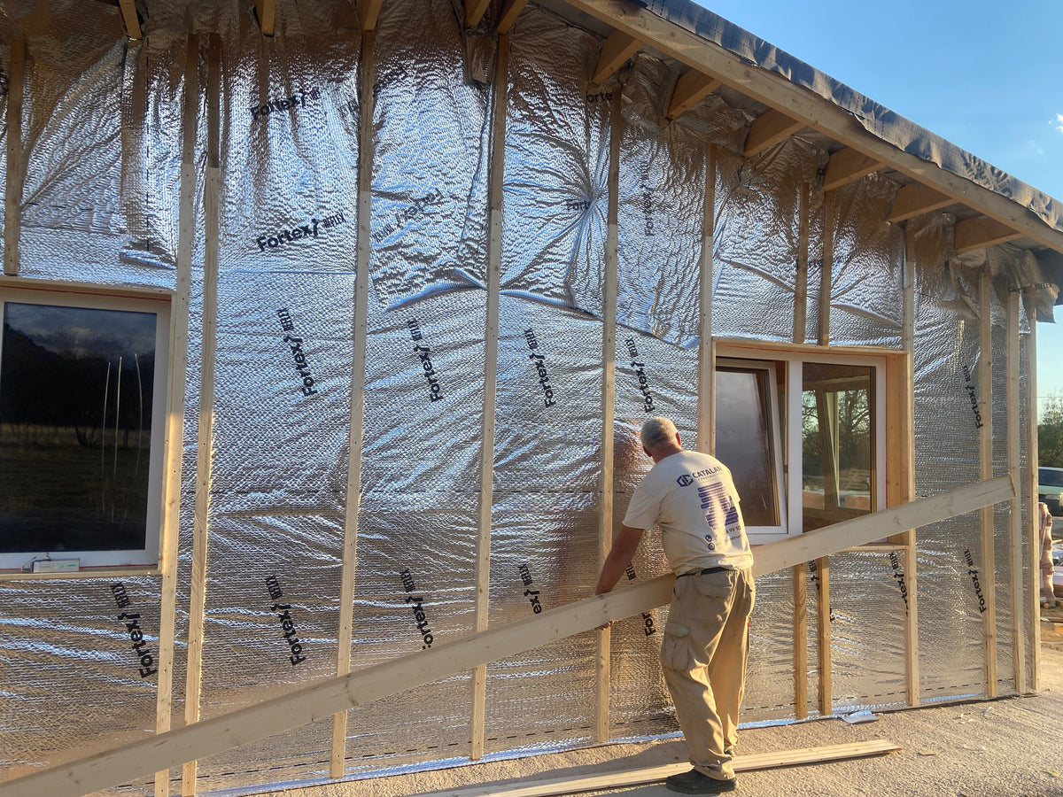 Operario de Catalan Construction junto a una fachada con aislamiento reflectante y rastreles de madera.