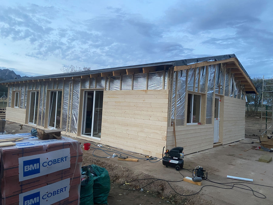 Fachada con revestimiento de madera parcialmente instalado y aislamiento todavía visible.