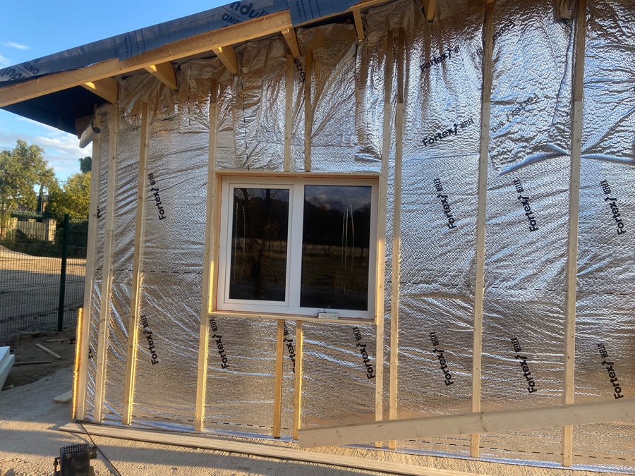 Ventana blanca rodeada de aislamiento reflectante y rastreles de madera durante la obra.